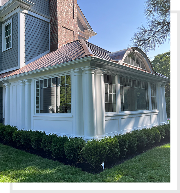 RE-IMG A white house with bushes around it and a green roof.